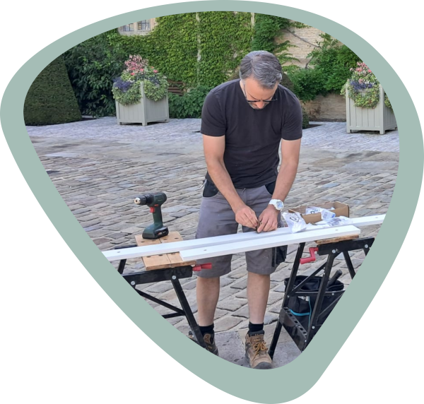 A handyman in the courtyard of a private estate looking down onto a trestle table with wood and tools.