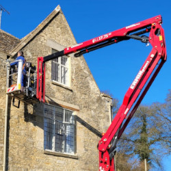 A handyman in a Cherry Picker inspecting gutters of a country house in the Cotswolds.